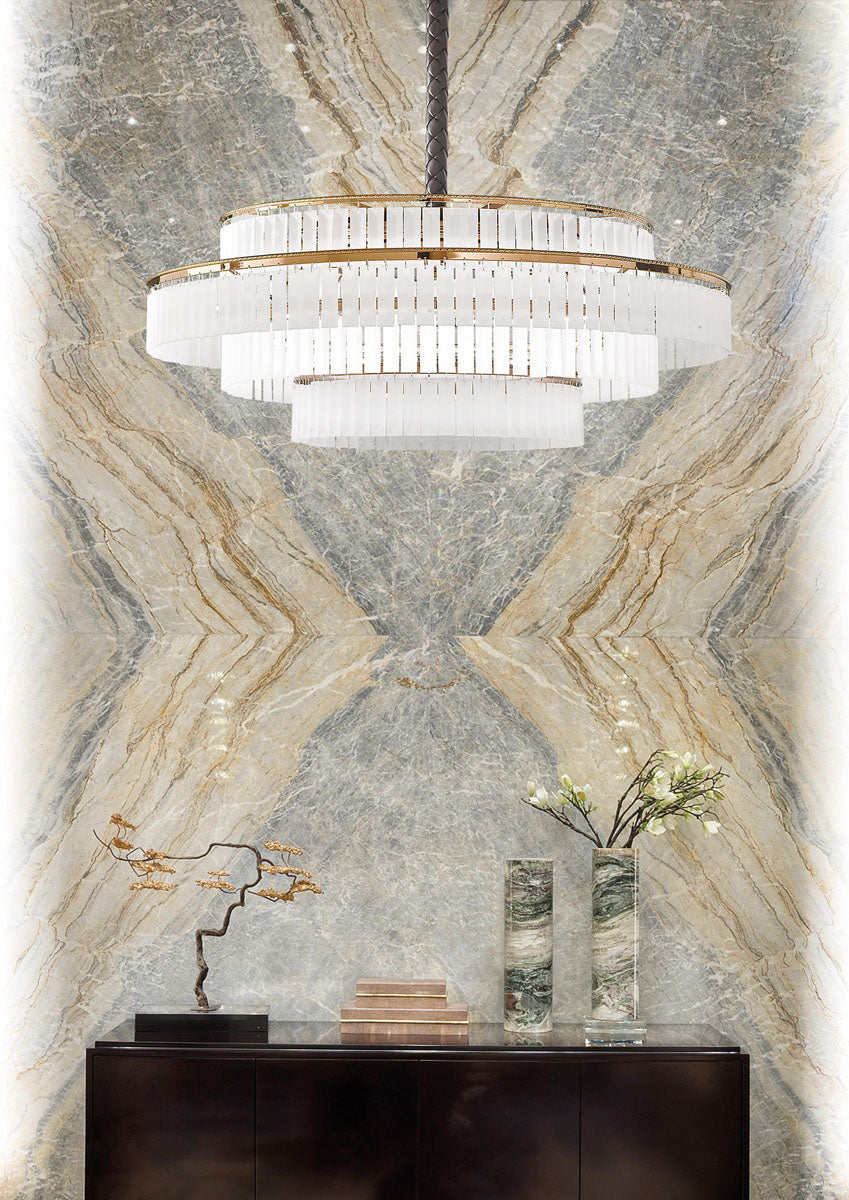 Charles Collection suspension lamp by Italamp featuring gold nickel finish, satin glass elements, and leather accents, epitomising Italian luxury lighting design. A Charles chandelier in front of a exquisite marble wall above a wooden side board styled with artefacts and objects