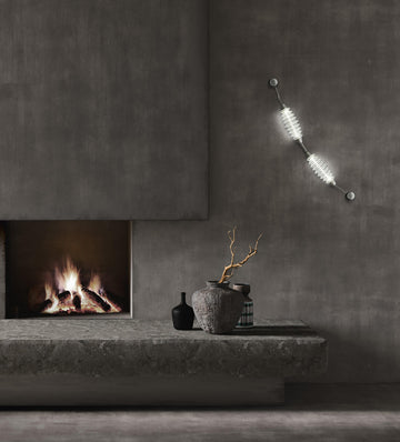 Colier collection by Italamp, featuring modular blown glass elements in vibrant colours and shapes, designed by Marc Sadler to create magical lighting effects. Set on a dark theme interior on the wall next to a fireplace and art objects