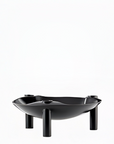 A black metal candle holder with a wide, shallow bowl shape and three short cylindrical legs, shown on a plain white background.