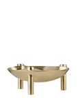 A modern three-legged metal candle holder with a shallow bowl shape and three cylindrical legs, finished in a brushed gold or brass-like metallic finish, shown on a plain white background.