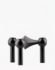 A modern three hole candle holder with a black finish, featuring three spherical shades on vertical cylindrical stems with a geometric central bar, shown against a plain white background. From Stoff Nagel Denmark, available at Spacio in India. 