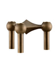 A modern three hole candle holder with a bronze finish, featuring three spherical shades on vertical cylindrical stems with a geometric central bar, shown against a plain white background. From Stoff Nagel Denmark, available at Spacio in India. 