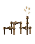 Bronze-finished geometric metal vase and candle holder with spherical and angular forms, shown on a plain white background with dried grass stems inserted into one of the vase openings.
