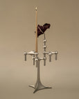 A modern silver-toned metal candelabra with a single tall beige candle and a dark dried rose, set against a solid warm beige background.