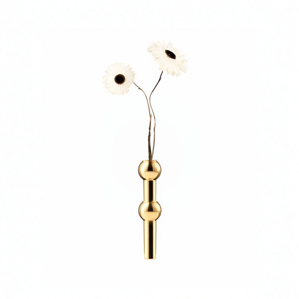 A minimalist brass metal vase with a vertical cylindrical body and two rounded decorative nodes, holding two artificial white daisy flowers with dark centers, set against a solid white background.