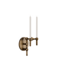 An antique bronze wall sconce with two candle-style arms holding white taper candles, shown against a plain white background.