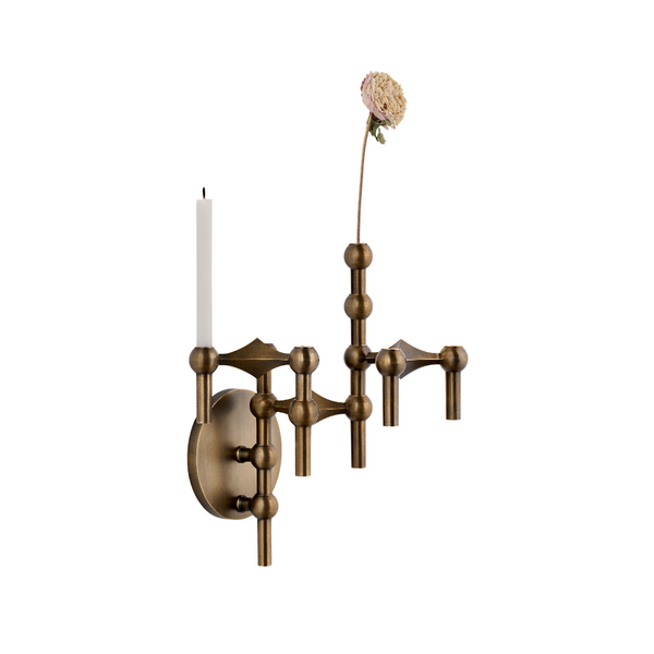 An ornate wall-mounted candle-style sconce in an antique brass finish, featuring a circular backplate, three branching arms with bead-like accents, a single white candle, and a tall dried flower stem extending upward, shown against a plain white background.