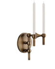 A wall-mounted candlelight fixture in an antique bronze finish, featuring a round backplate and two vertical arms holding white taper candles, shown against a plain white background.