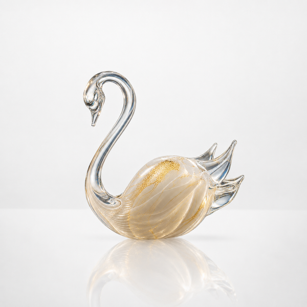 A decorative crystal swan figurine with a curved neck, clear glass body, and subtle gold flecks, displayed on a reflective white surface against a light gray background.