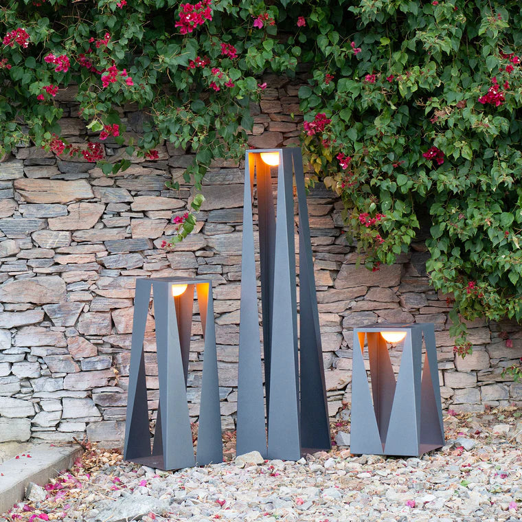 Decorative outdoor lantern with a stone wall and flowering plants in the background by Les Jardins from Spacio retail stores in India. 