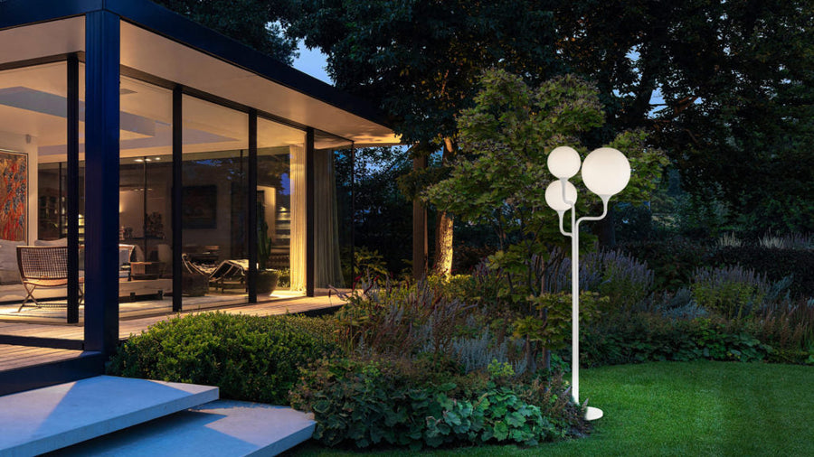 Modern outdoor garden light fixture in a residential setting with a house and garden.