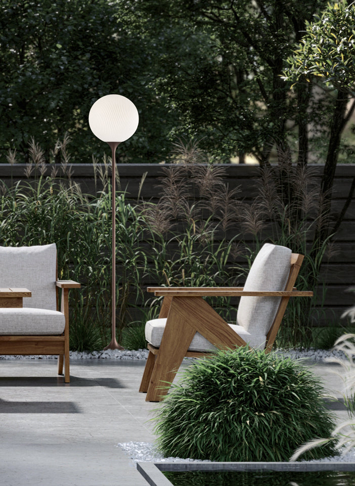 Outdoor setting with wooden chairs, a floor lamp, and greenery.