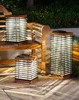 Solar-powered outdoor lanterns on a wooden bench in a garden setting by Les Jardins available at Spacio in India. 