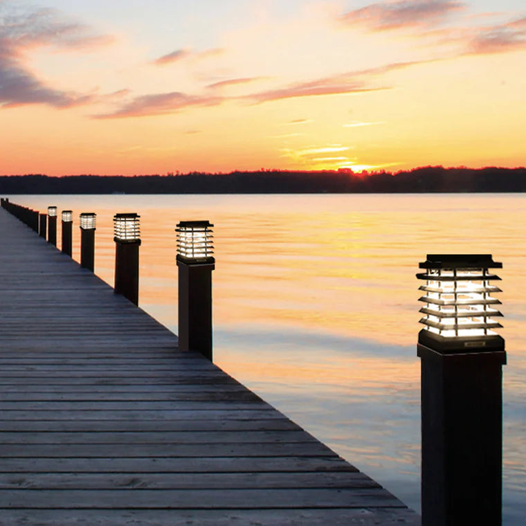 Wooden dock with illuminated solar lamp posts extending into a body of water at sunset by Les Jardins available at Spacio retail stores in Mumbai & Kolkata. 