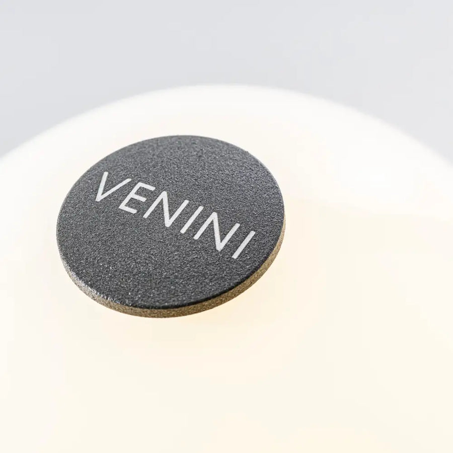 Round dark metal with 'VENINI' branding on a light gray background on the bottom of Fantasmino table lamp from Venini at Spacio store in Mumbai