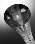 A close-up studio shot of a clear glass vase with a wide circular opening, textured interior ridges, and a tapered base, shown against a dark-to-light gray gradient background.