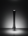A sleek, glossy black sculptural glass vase with a flared base, standing upright on a reflective surface against a dark gray gradient background.