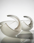 Two modern sculptural bowls in a glossy white finish, shown on a reflective light gray surface against a clean white studio background.