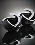 Two glossy black decorative glass objects with curved white accents, arranged on a reflective dark surface against a gray gradient background.