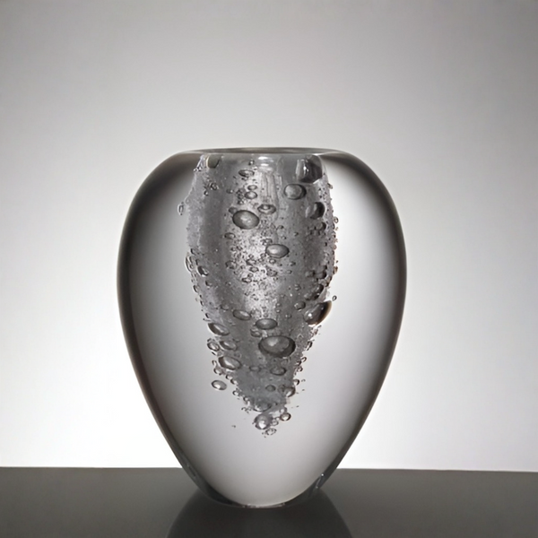 A sculptural glass vase with a rounded teardrop shape, featuring a textured, bubble-filled vertical column on the front, set against a neutral gray gradient background.