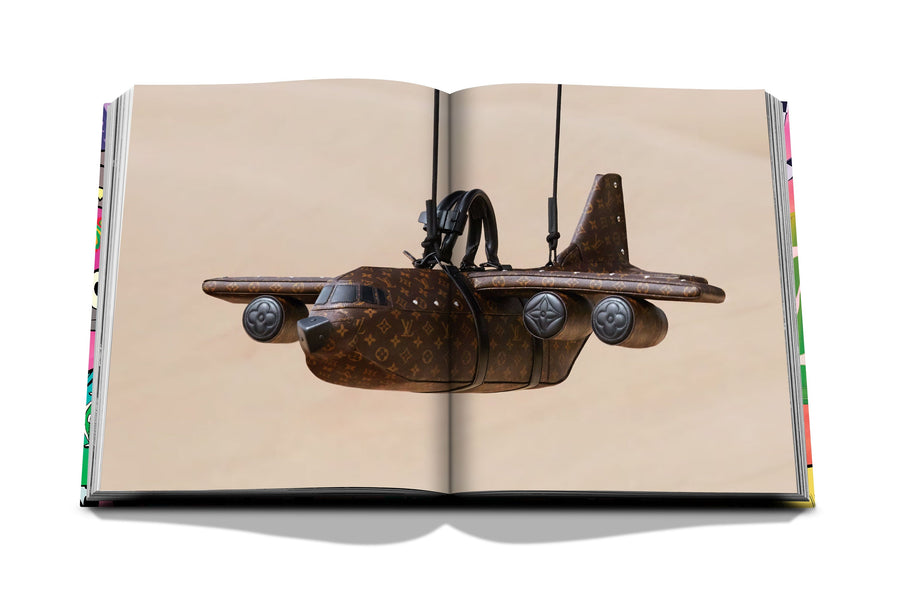 Assouline Louis Vuitton: Virgil Abloh Classic Cartoon Cover coffee table book displaying photo of Louis Vuitton Airplane Bag woth Rs. 28 Lacs on a white back ground available at Spacio India for luxury home decor accessories collection of Fashion Coffee Table Books.