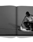 Assouline Louis Vuitton: Virgil Abloh Classic Cartoon Cover coffee table book displaying Grey Image of Virgil Abloh using Apple Mac Laptop on a white back ground available at Spacio India for luxury home decor accessories collection of Fashion Coffee Table Books.