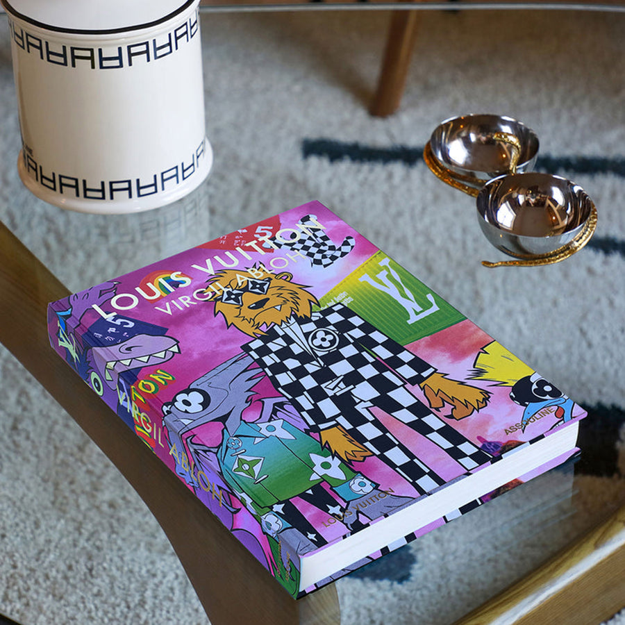 Assouline Louis Vuitton: Virgil Abloh Classic Cartoon Cover coffee table book on glass table with other home accessories available at Spacio India for luxury home decor accessories collection of Fashion Coffee Table Books.