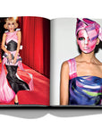 Assouline Moschino coffee table book displaying photos of Model Gigi Hadid wearing a baby doll dress & a model painted her face for fashion runway on a white back ground available at Spacio India for luxury home decor accessories collection of Fashion Coffee Table Books.