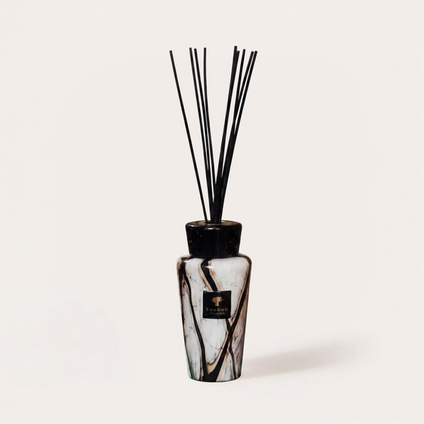 A reed diffuser bottle with a black and white marble pattern, featuring a black cap and several black reeds, on a light beige background.