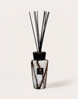 A reed diffuser bottle with a black and white marble pattern, featuring a black cap and several black reeds, on a light beige background.