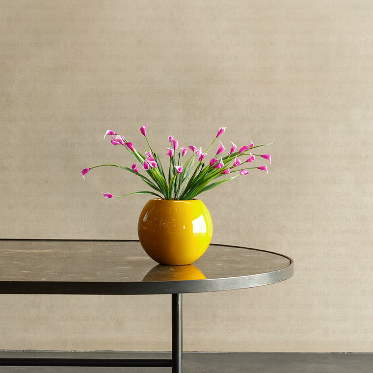 Yellow vase with pink flowers on a black table against a beige wall