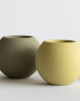 Three textured ceramic pots in green, yellow, and beige on a light background