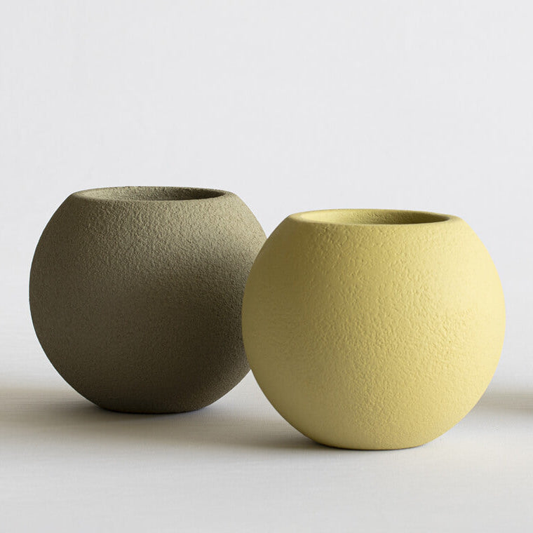 Three textured ceramic pots in green, yellow, and beige on a light background