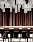 Modern chandelier hanging above a bar with stools against a dark wall.