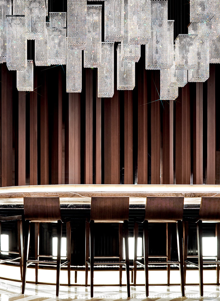 Modern chandelier hanging above a bar with stools against a dark wall.