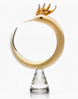 Decorative object resembling a Phoenix with gold antlers on a clear base against a white background