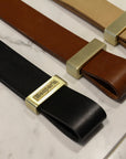 Three Esperia Eredania Horizontal leather belts with gold buckles on a marble counter.