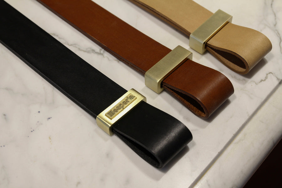Three Esperia Eredania Horizontal leather belts with gold buckles on a marble counter.