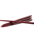 Six dark red taper candles crossed over each other on a plain white background from Ester & Erik available at Spacio in India.