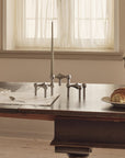 A matte black metal three legged candle holder, styled on a dark wooden table in a warm, neutral-toned kitchen setting.