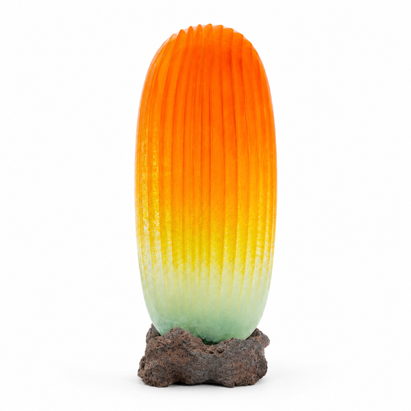 A ribbed glass sculpture with a vibrant orange and yellow gradient fading to a pale mint green at the base, set on a rustic dark brown stone pedestal against a white background.