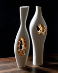Two white and gold vases on a wooden table, including the Fos Ceramiche Falling in Love Gold Vase (Pair) by Enea Mazzotti.