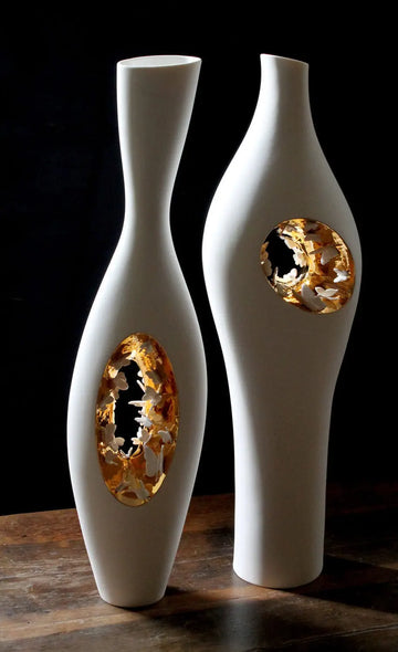 Two white and gold vases on a wooden table, including the Fos Ceramiche Falling in Love Gold Vase (Pair) by Enea Mazzotti.