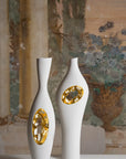 Two white and gold Fos Ceramiche Falling in Love Gold Vase (Pair) on a table in front of a painting.