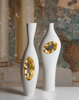 Two white and gold Fos Ceramiche Falling in Love Gold Vase (Pair) on a table in front of a painting.