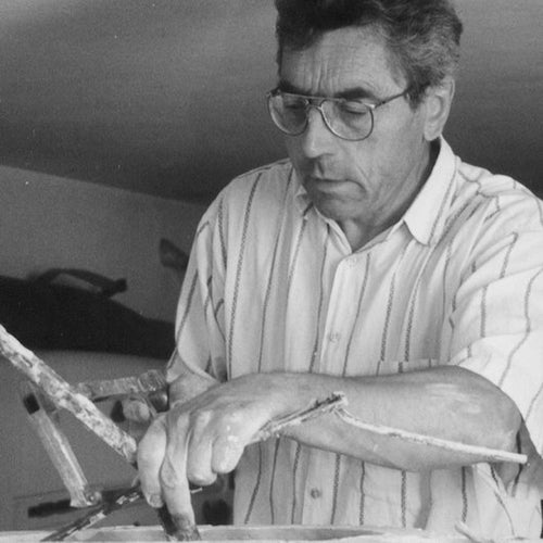 An old black and white photo of a man skillfully working on a piece of wood, creating intricate details with precision and expertise with the Gardeco Ceramic Sculpture Visitor Small Sand Cor02 from Gardeco.