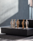 A collection of Gardeco Ceramic Sculpture Visitor Small Cinza Cor25 figurines, created by a Belgian sculptor, showcasing intricate details and a beautiful Cinza finish, placed on a black table.