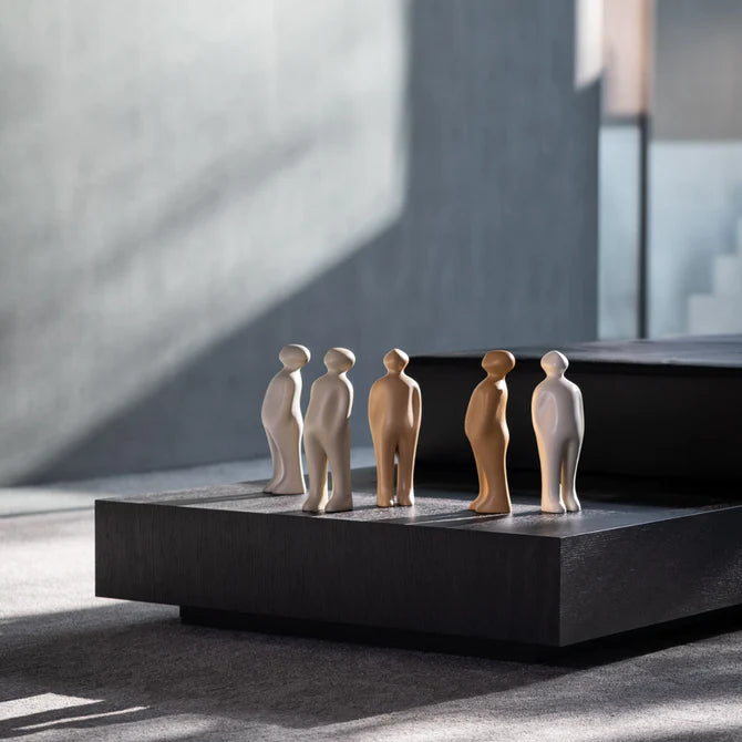 A collection of Gardeco Ceramic Sculpture Visitor Small Taupe Cor27 figurines, crafted by a Belgian sculptor, displayed on a sleek black table.
