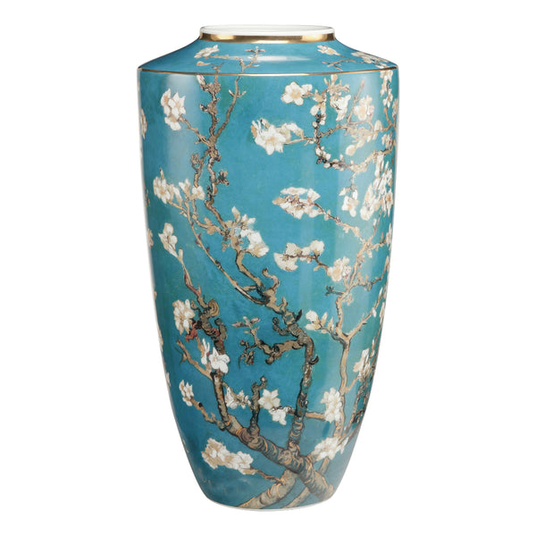 A tall ceramic vase with a turquoise blue background and a detailed print of white blossoms on branching tree trunks, finished with a thin gold rim at the top, shown on a plain white background. Artwork of Vincent van Gogh by Goebel available at Spacio in India. 