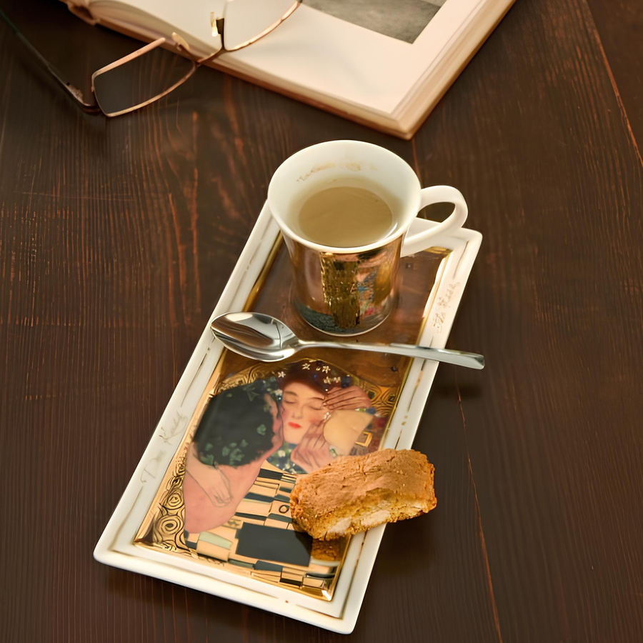 Goebel The Kiss Espresso Set of tea cup & saucer by Gustav Klimt on a wooden table with a spoon available at Spacio India for luxury home decor collection of Tableware accessories.